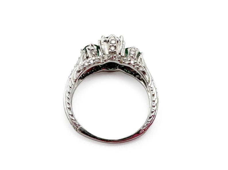 May include: A silver ring with three emerald green stones and a decorative filigree design.