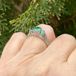 May include: A silver ring with a delicate filigree design and three emerald green gemstones.