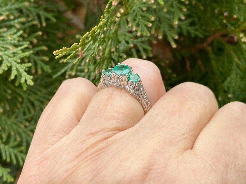 May include: A silver ring with a delicate filigree design and three emerald green gemstones.