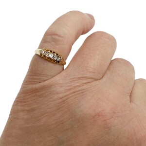 May include: A gold ring with five small diamonds set in a row. The ring is on a person's finger.