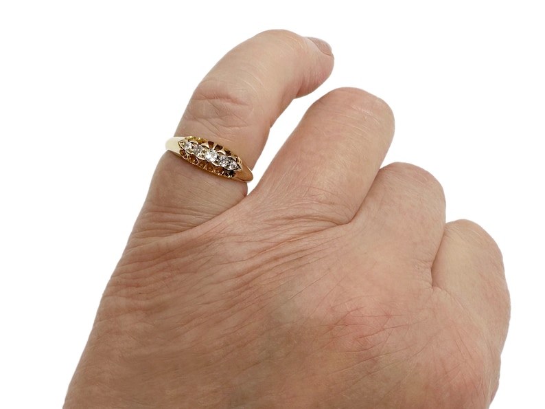 May include: A gold ring with five small diamonds set in a row. The ring is on a person's finger.