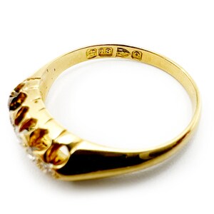 May include: A gold band ring with five small diamonds set in a row. The ring is marked "18 15 3 Q" on the inside.