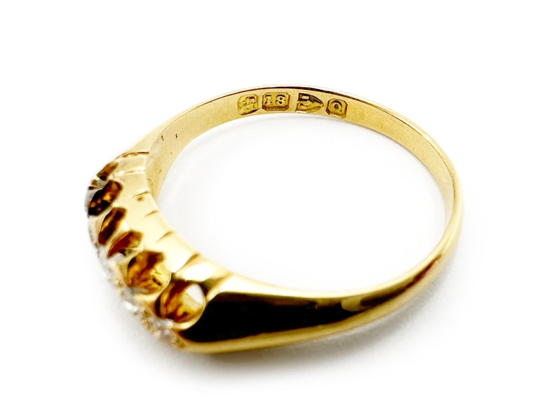 May include: A gold band ring with five small diamonds set in a row. The ring is marked "18 15 3 Q" on the inside.