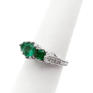 May include: A silver ring with a row of five emerald green gemstones set in a decorative band.