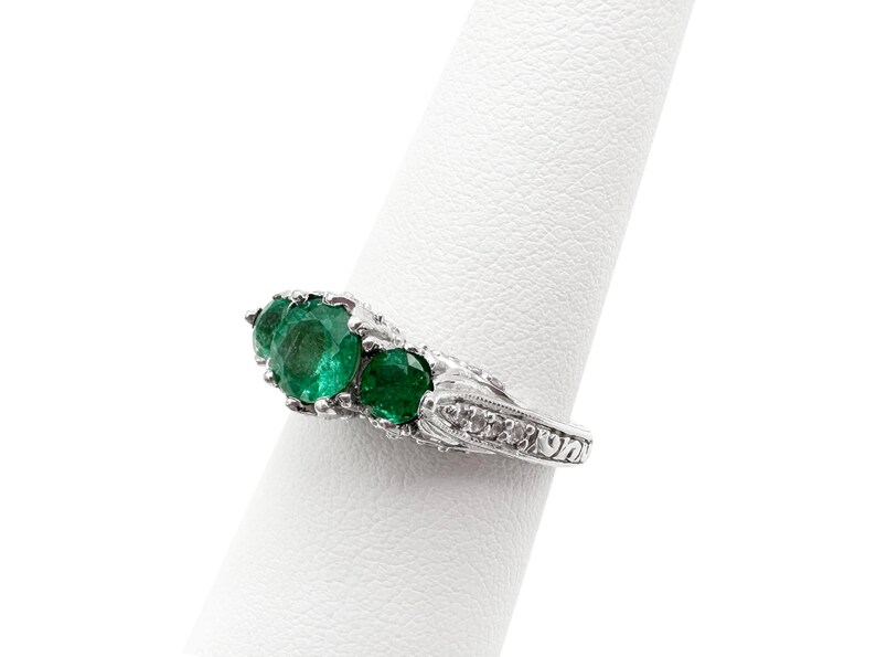 May include: A silver ring with a row of five emerald green gemstones set in a decorative band.