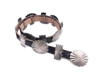 May include: A black leather belt with silver floral-shaped conchos. The belt has a buckle with a silver floral design.