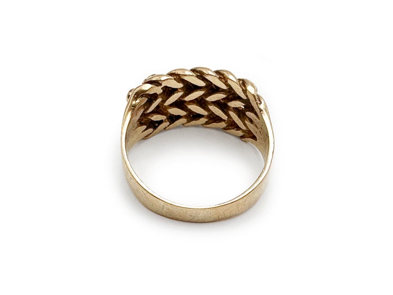 K&ouml;nnte beinhalten: Ein goldener Ring mit einem geflochtenen Design. Der Ring besteht aus einem dicken Metallband und hat eine glatte Oberfl&auml;che.