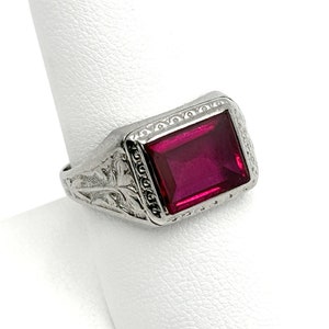 May include: A silver ring with an ornate design and a large, square, dark red gemstone.