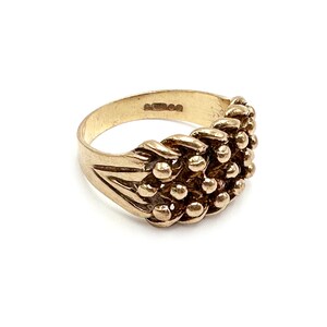 K&ouml;nnte beinhalten: Ein goldener Ring mit einem strukturierten Design aus kleinen, runden Perlen. Der Ring besteht aus einem dicken Band und hat eine leicht abgerundete Form.