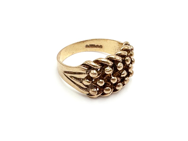K&ouml;nnte beinhalten: Ein goldener Ring mit einem strukturierten Design aus kleinen, runden Perlen. Der Ring besteht aus einem dicken Band und hat eine leicht abgerundete Form.