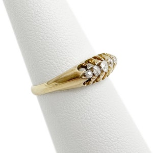 May include: A gold band ring with a row of small, clear diamonds set in a curved design.