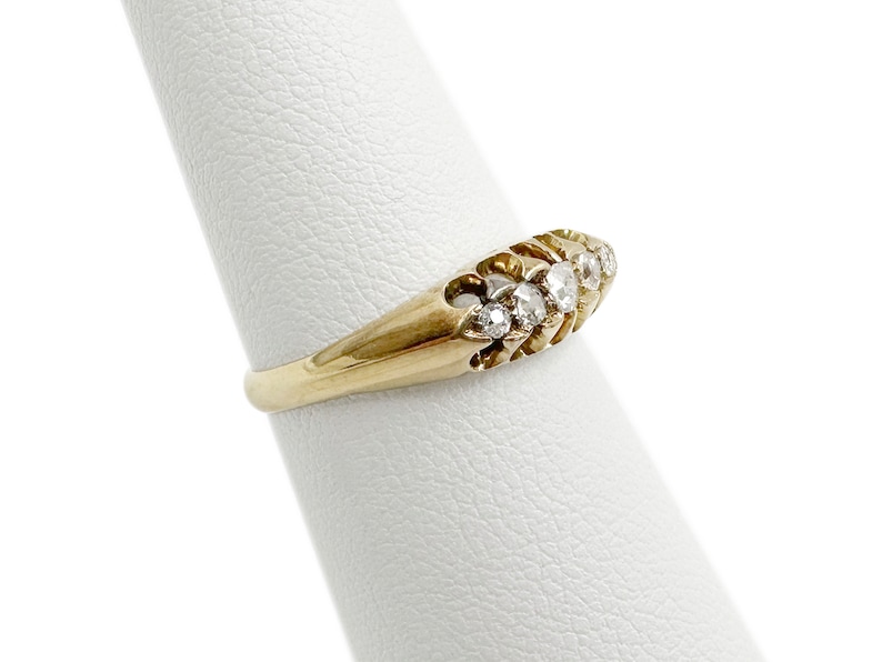 May include: A gold band ring with a row of small, clear diamonds set in a curved design.