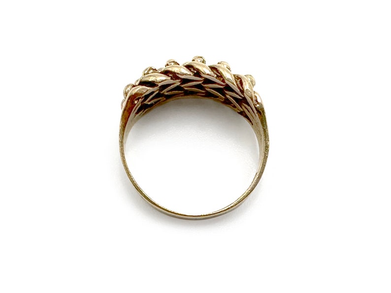 K&ouml;nnte beinhalten: Ein goldener Ring mit geflochtenem Design. Der Ring besteht aus einer Reihe von ineinandergreifenden Schlaufen, die eine strukturierte Oberfl&auml;che erzeugen.
