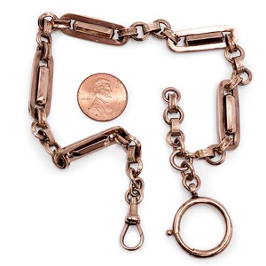 May include: A gold-toned pocket watch chain with a swivel clasp and a rectangular link design. The chain is about the size of a US penny.