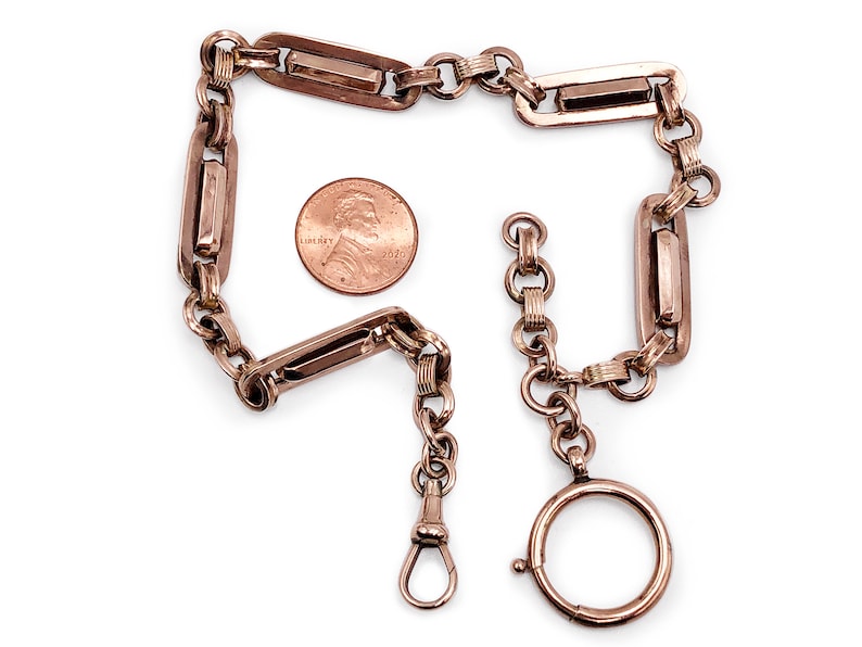 May include: A gold-toned pocket watch chain with a swivel clasp and a rectangular link design. The chain is about the size of a US penny.