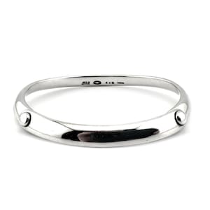 May include: A polished silver bangle bracelet featuring a smooth, tapered band with two small, raised circular studs on opposite sides. The interior of the band is engraved with the text 925, a hallmark symbol, 440, and the word TORUN.