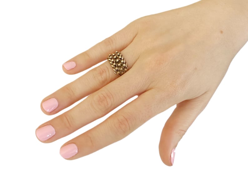 K&ouml;nnte beinhalten: Ein goldener Ring mit einem strukturierten Design. Der Ring besteht aus kleinen, runden Perlen, die zusammengef&uuml;gt sind.