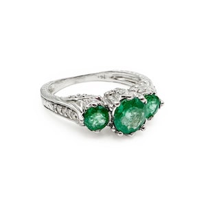 May include: A silver ring with three emerald green gemstones set in a delicate, intricate design. The ring is accented with small, sparkling diamonds.