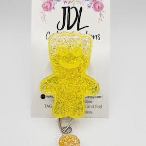 May include: Yellow glitter gummy bear shaped retractable badge holder with a clear plastic badge holder and a silver spring.