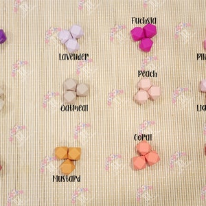 May include: A set of 12 silicone teethers in various colors, including purple, lavender, fuchsia, pink, light pink, tan, oatmeal, peach, coral, red, maroon, and mustard. The teethers are shaped like a geometric figure with multiple sides.