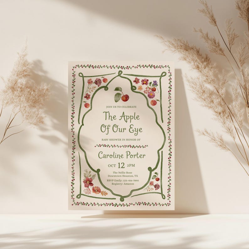 Puede incluir: Una tarjeta de invitaci&oacute;n rectangular para baby shower con un borde verde dibujado a mano y bayas rojas. El texto dice The Apple Of Our Eye, en honor a Caroline Porter el 12 de octubre a las 2 PM en The Nellie Rose en Houston, Texas.