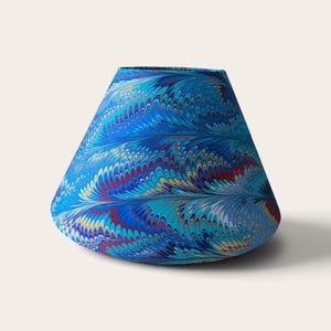 May include: A tapered, wide-bottomed vase featuring a vibrant marbled pattern. The surface displays intricate, swirling designs in shades of deep blue, bright turquoise, red, and yellow, creating a dense, feather-like texture across the exterior.