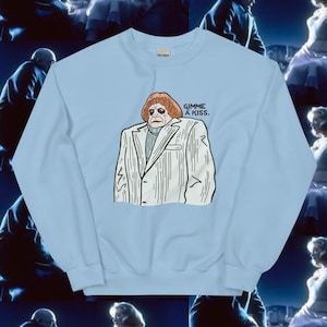 May include: Light blue sweatshirt featuring a cartoon illustration of a man in a white suit with the text "Gimme a kiss." printed on the front.