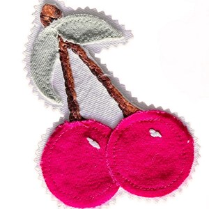May include: A fabric patch featuring two bright pink circular cherries with brown embroidered stems and a light green leaf. The design is outlined with a white zigzag edge, creating a distinct border around the cherry shape on a white background.