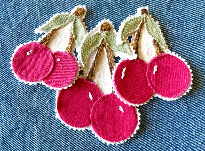 May include: Three fabric cherry patches featuring bright pink circular fruit, brown embroidered stems, and light green leaves. Each cherry pair is set against a white scalloped fabric backing with visible white stitching highlights on the fruit.