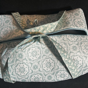 May include: A rectangular fabric bag featuring a light teal and white geometric mandala pattern. The bag includes two handles made from a contrasting light teal fabric decorated with a small white floral print, attached to the top.