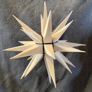 May include: A white paper star with black string, hanging from the ceiling. The star is made of many points and has a 3D effect.