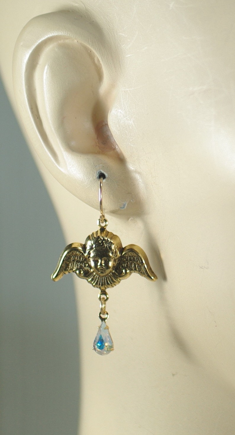 Pu&ograve; includere: Orecchini a forma di angelo color oro con viso di cherubino e ali. Ogni orecchino presenta una gemma a goccia iridescente pendente. Gli orecchini sono progettati per orecchie forate.
