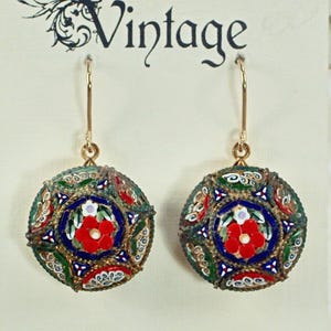 May include: A pair of vintage mosaic earrings. Each earring features a round, gold-toned frame with a colorful mosaic design. The mosaic includes red, blue, green, and white floral patterns. The word "Vintage" is above the earrings.