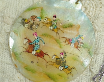 May include: A pearlescent shell pendant with a painted scene of riders on horseback. The riders wear colorful clothing and ride across a landscape of green hills. The pendant hangs from a silver-colored chain.