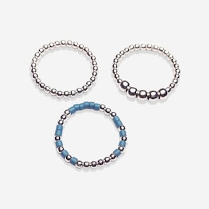 May include: Three silver bead bracelets. One bracelet has blue beads interspersed with the silver beads.