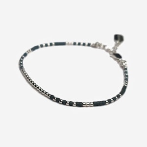 May include: A delicate bracelet made with small black and silver beads. The bracelet has a silver clasp.