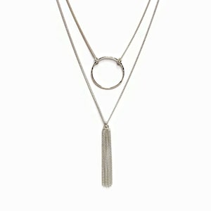 Peut inclure: Un collier argenté à plusieurs rangs avec un pendentif rond et un charme en forme de pompon.