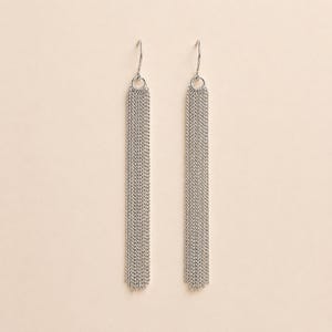 Puede incluir: Un par de pendientes colgantes de color plateado. Cada pendiente presenta un pequeño gancho en la parte superior, conectado a un diseño de cadena circular. Debajo, una larga cascada rectangular de cadenas finas cuelga, creando un efecto de flecos. Los pendientes se muestran sobre un fondo neutro.