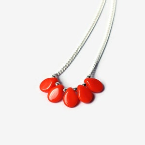 Puede incluir: Un collar con una cadena de tono plateado y cinco cuentas lisas en forma de l&aacute;grima de un color rojo anaranjado vibrante. Las cuentas est&aacute;n dispuestas en un grupo en el centro de la cadena, separadas por peque&ntilde;as cuentas espaciadoras met&aacute;licas.