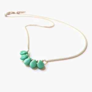Puede incluir: Un collar de cadena en tono dorado con cinco cuentas lisas en forma de l&aacute;grima de color turquesa dispuestas en un grupo en el centro. La delicada cadena de metal incluye un peque&ntilde;o mecanismo de cierre en el extremo, con un dise&ntilde;o sencillo.