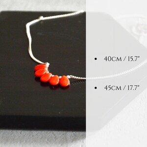 Puede incluir: Un collar de cadena plateada con cinco cuentas de color naranja vibrante en forma de l&aacute;grima dispuestas en racimo. El texto a la derecha indica dos opciones de longitud: 40 cm / 15,7 pulgadas y 45 cm / 17,7 pulgadas, proporcionando informaci&oacute;n de tama&ntilde;o.