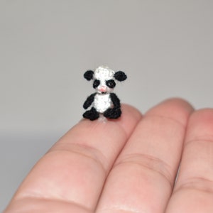 Puede incluir: Un pequeño oso panda de crochet con orejas, ojos y patas negras, sentado en una mano.
