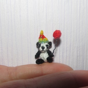 Puede incluir: Un pequeño panda de crochet con un gorro de fiesta colorido y sosteniendo un globo rojo.