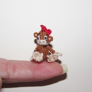 May include: A small crocheted monkey toy with brown fur, white hands and feet, and a red bow on its head.