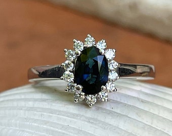 May include: A silver ring with a dark blue oval sapphire surrounded by a halo of small diamonds.