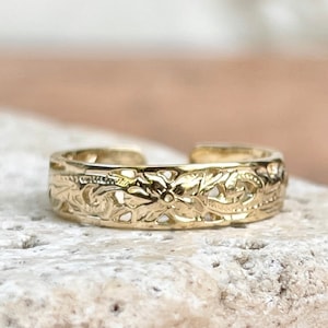 May include: A gold toe ring with a delicate floral design.