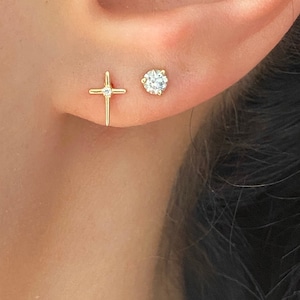 May include: A pair of gold earrings, one with a small diamond and the other with a small cross.