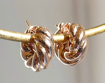 May include: A pair of rose gold knot-shaped hoop earrings. The earrings are made of a twisted metal design.