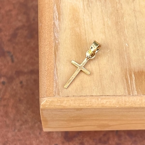 May include: A small gold cross pendant charm. The cross is simple and elegant, with a smooth finish.