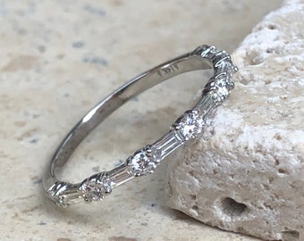 May include: A silver band ring with a row of small, clear baguette-shaped diamonds set in a pave setting.
